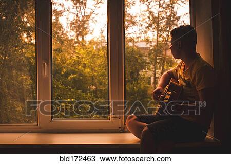 Stock Image - Caucasian man playing guitar in window sill. Fotosearch