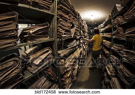 Stock Photo - Caucasian man searching old newspapers in library archive. Fotosearch
