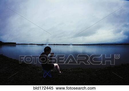 Stock Photography - Caucasian man sitting by remote lake. Fotosearch