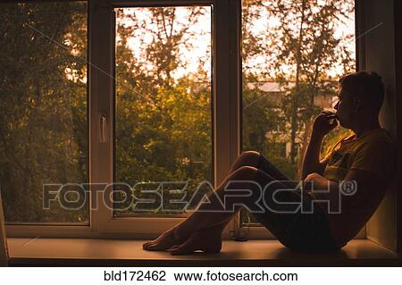 Stock Image - Caucasian man sitting in window sill. Fotosearch