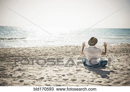 Stock Image - Caucasian man sitting on beach. Fotosearch