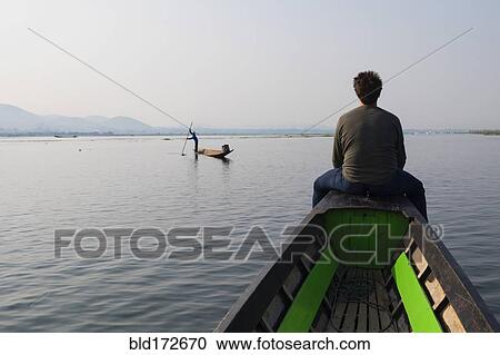 Stock Image - Caucasian man sitting on canoe on rural lake. Fotosearch
