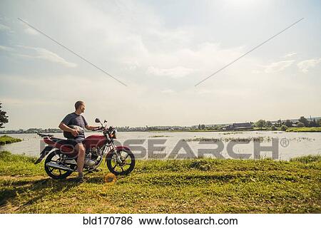 Caucasian man sitting on motorcycle in park View Large Photo Image Stock Photograph - Caucasian man sitting on motorcycle in park. Fotosearch