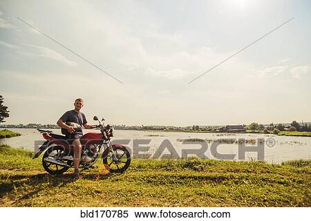 Stock Photography - Caucasian man sitting on motorcycle in park. Fotosearch