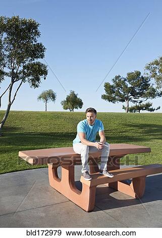 Stock Photo - Caucasian man sitting on picnic table in park. Fotosearch