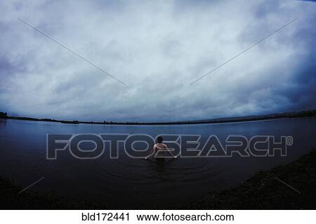 Stock Image - Caucasian man standing in still remote lake. Fotosearch