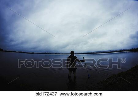 Stock Photo - Caucasian man standing in still remote lake. Fotosearch