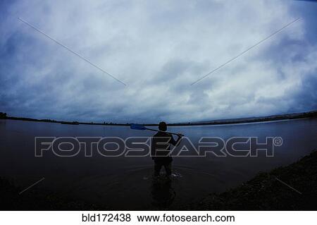 Stock Photo - Caucasian man standing in still remote lake. Fotosearch