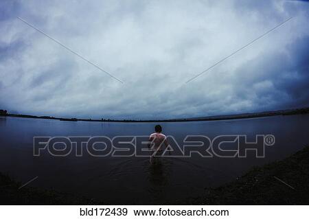 Stock Photo - Caucasian man standing in still remote lake. Fotosearch