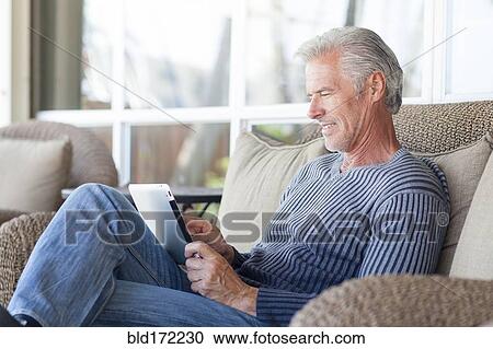 Stock Image - Caucasian man using digital tablet on sofa. Fotosearch