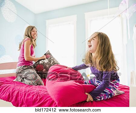 Stock Image - Caucasian mother and daughter having pillow fight on bed. Fotosearch