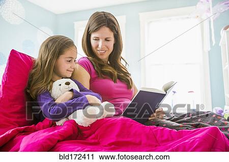 Stock Image - Caucasian mother and daughter reading in bed. Fotosearch
