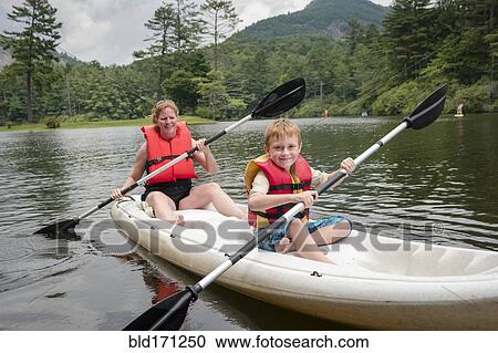Stock Image - Caucasian mother and son rowing canoe in lake. Fotosearch