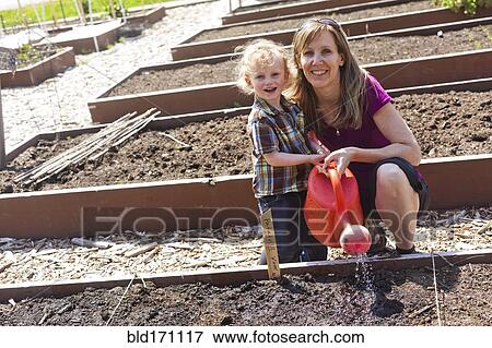 Stock Photo - Caucasian mother and son watering plants in garden. Fotosearch