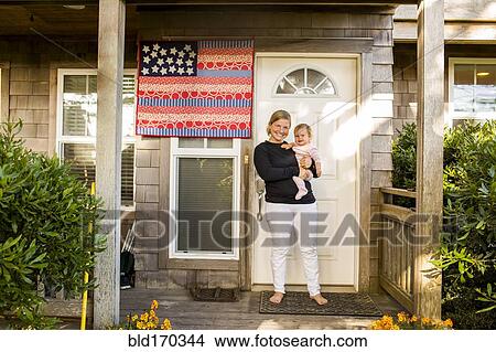 Picture - Caucasian mother holding baby daughter on front porch. Fotosearch