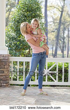 Stock Image - Caucasian mother holding daughter on patio. Fotosearch