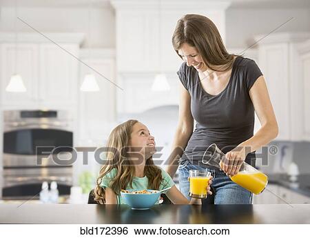 Stock Photograph - Caucasian mother pouring juice for daughter in kitchen. Fotosearch