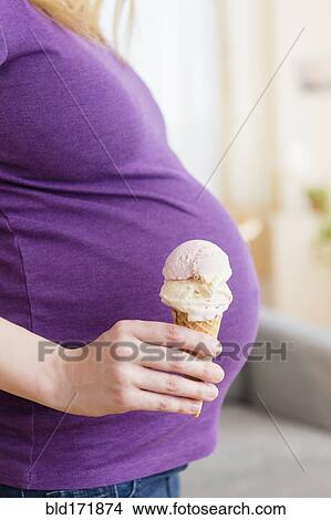 Picture - Caucasian pregnant woman holding ice cream cone. Fotosearch