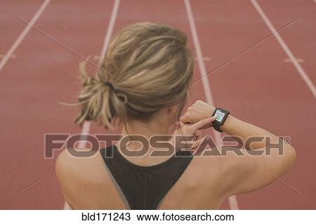 Stock Image - Caucasian runner checking watch on sports field. Fotosearch