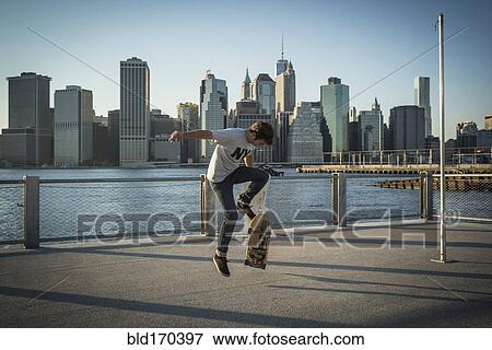 Stock Photo - Caucasian skateboarder doing trick at waterfront, New York, United States. Fotosearch