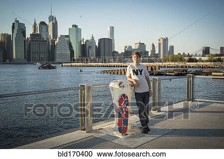 Stock Image - Caucasian skateboarder smiling at waterfront, New York, United States. Fotosearch