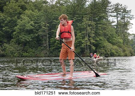 Stock Image - Caucasian teenage boy rowing paddleboat in lake. Fotosearch