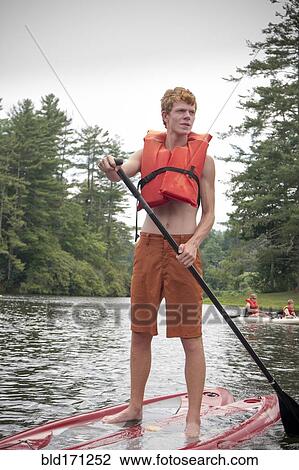 Stock Image - Caucasian teenage boy rowing paddleboat in lake. Fotosearch