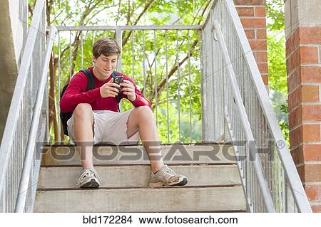 Picture - Caucasian teenage boy using cell phone on steps. Fotosearch