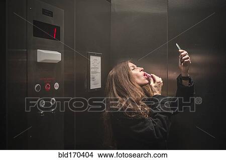 Picture - Caucasian woman applying lipstick in elevator. Fotosearch