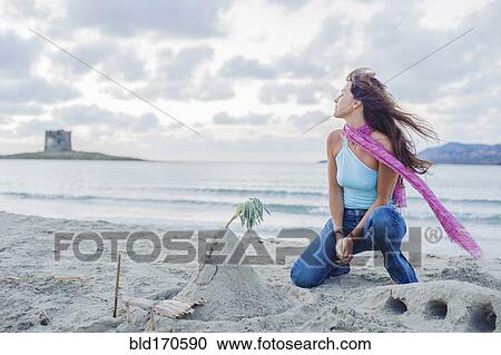 Stock Image - Caucasian woman building sandcastle on beach. Fotosearch