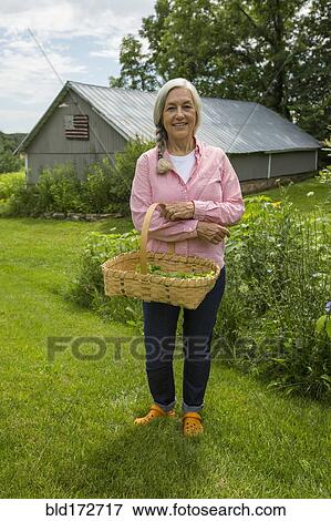 Stock Photo - Caucasian woman carrying basket of vegetables in garden. Fotosearch