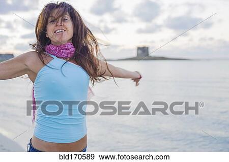 Stock Photo - Caucasian woman cheering on beach with arms outstretched. Fotosearch
