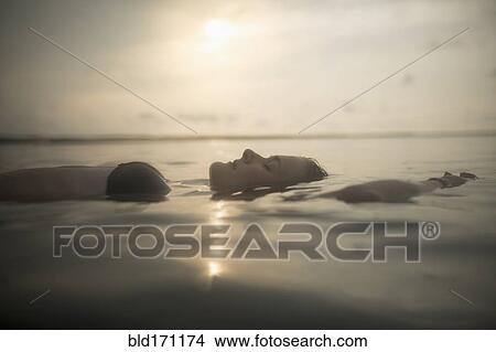 Picture - Caucasian woman floating in still lake. Fotosearch