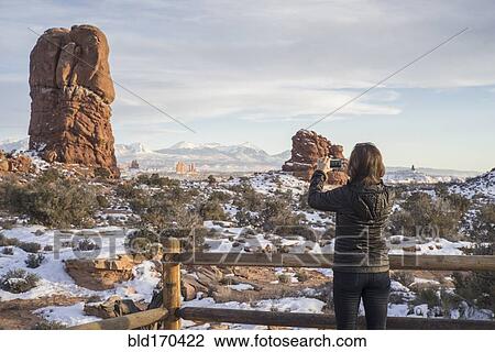 Stock Image - Caucasian woman photographing rock formations in landscape. Fotosearch