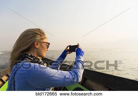 Stock Photography - Caucasian woman photographing rural lake from canoe. Fotosearch
