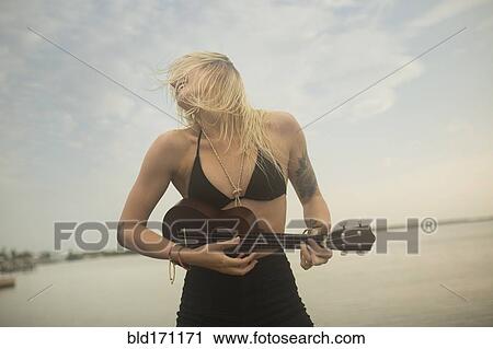 Stock Image - Caucasian woman playing ukulele on beach. Fotosearch