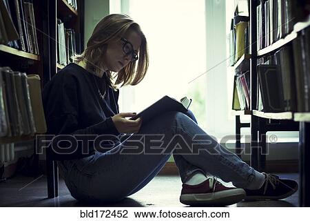 Stock Image - Caucasian woman reading book in library. Fotosearch