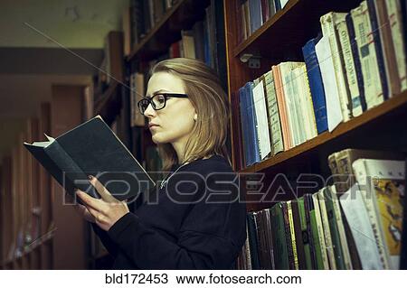 Stock Image - Caucasian woman reading book in library. Fotosearch