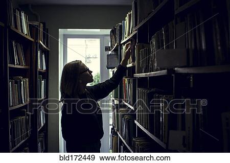 Stock Photo - Caucasian woman searching for book in library. Fotosearch