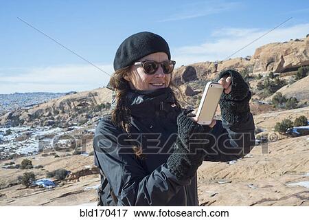 Stock Photo - Caucasian woman taking cell phone photograph on hillside. Fotosearch