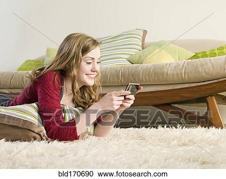Stock Image - Caucasian woman using cell phone on carpet. Fotosearch