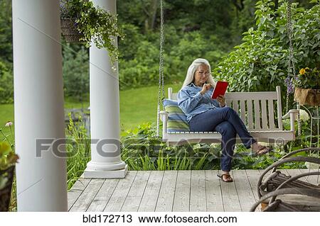 Stock Image - Caucasian woman using digital tablet on porch swing. Fotosearch