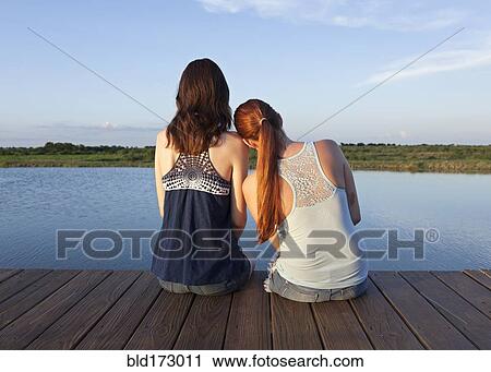 Stock Image - Caucasian women sitting on wooden dock over lake. Fotosearch
