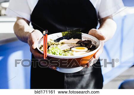 Stock Image - Chef holding bowl of ramen in restaurant. Fotosearch