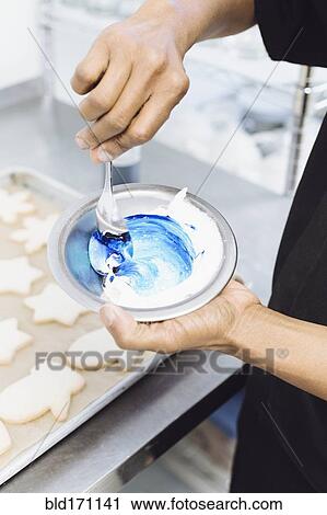 Stock Image - Close up of baker making blue frosting in bakery. Fotosearch