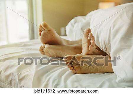 Stock Image - Close up of feet of couple in bed. Fotosearch