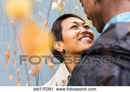 Stock Image - Close up of smiling couple standing in autumn leaves. Fotosearch