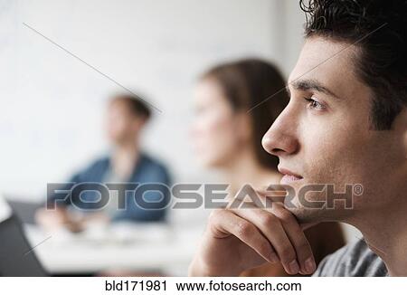 Stock Image - Close up of student listening in college classroom. Fotosearch