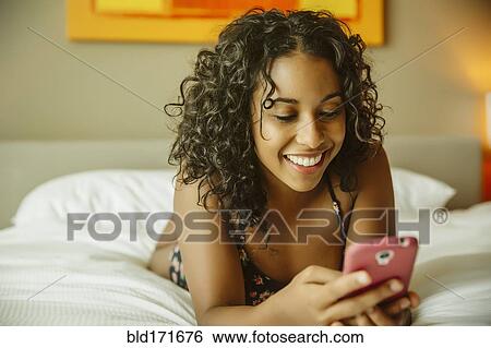 Stock Photograph - Close up of woman using cell phone on hotel bed. Fotosearch