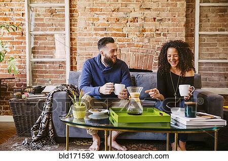 Couple drinking coffee on sofa in living room View Large Photo Image Stock Image - Couple drinking coffee on sofa in living room. Fotosearch